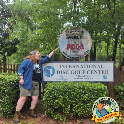 A red-haired woman standing next to the professional disc golf association center sign